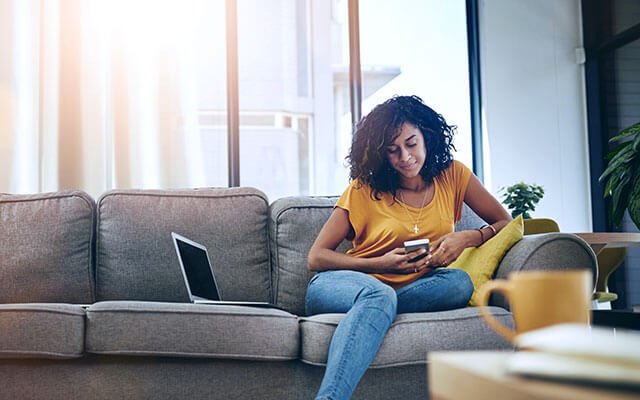 person on laptop and mobile on sofa