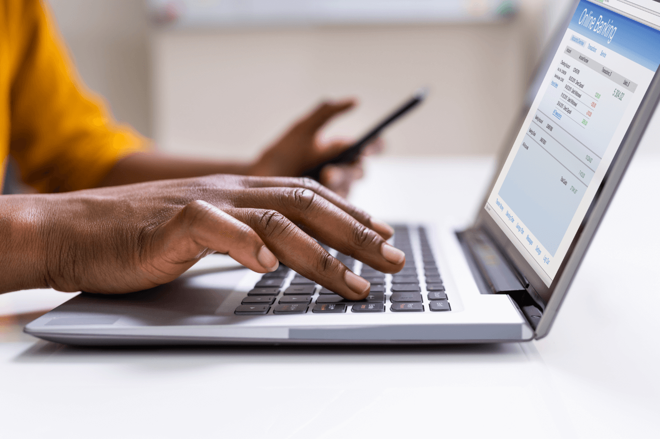 close up of hands typing on a laptop with one hand holding a credit card; digital banking is on the laptop screen